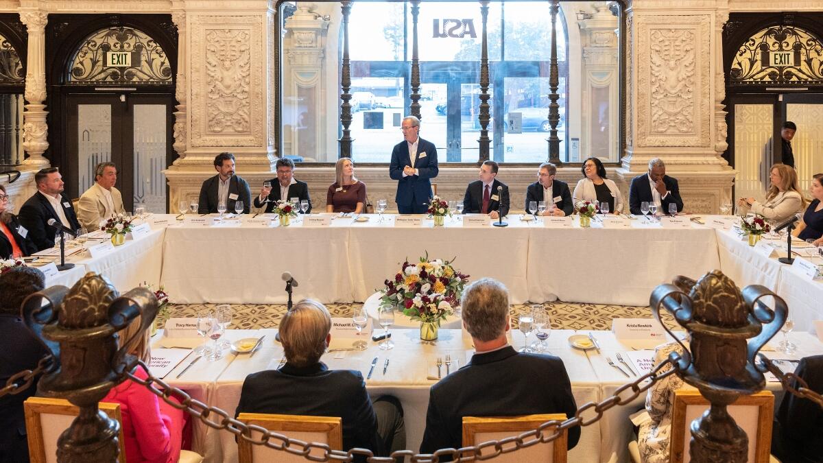 Nearly 30 higher education, community, business and media representatives sit at tables organized as a square in the lobby of the former Herald Examiner Building (now ASU in California) in Los Angeles
