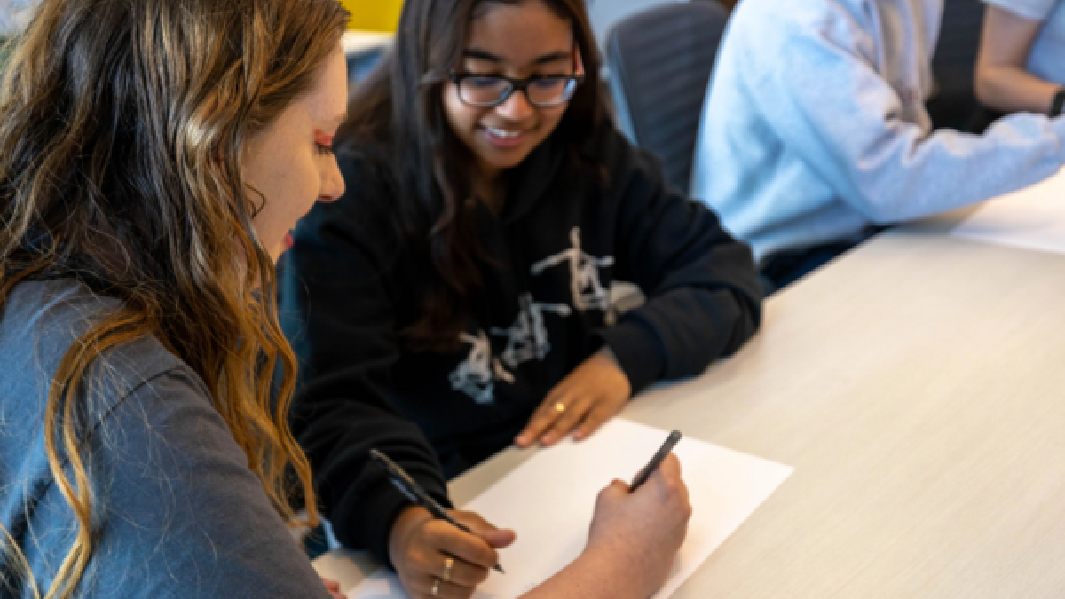 Two college students fill out paperwork while seated at a table.