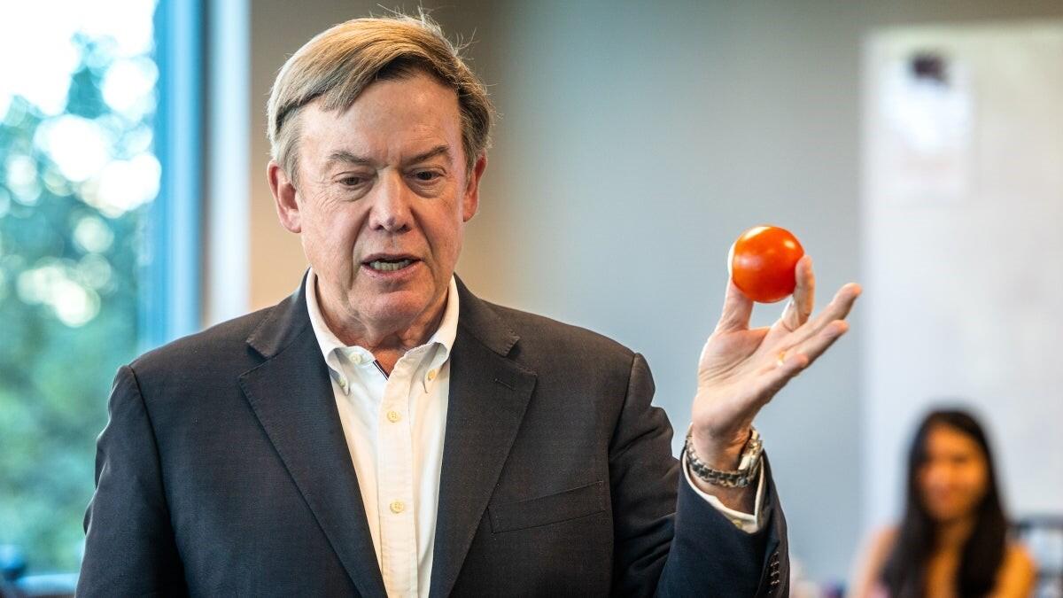 A person in a white shirt and gray blazer holds up a tomato during a course lecture on innovation.