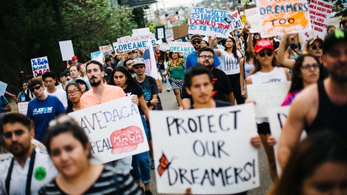 A large group of people march on a street holding handmade signs in support of the Dream Act and students. 